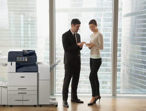 Zwei Personen in Geschäftskleidung diskutieren Dokumente in einem Büro neben einem Multifunktionsdrucker der Serie Xerox® AltaLink® B8200